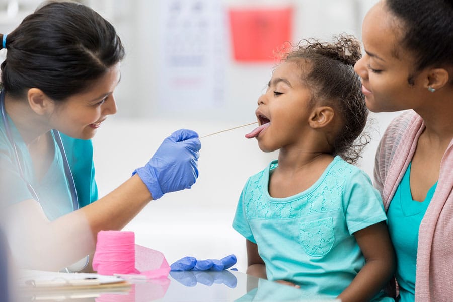 Provider examining a young child seated on her mother’s lap at urgent care Provider examining a young child seated on her mother’s lap at urgent care